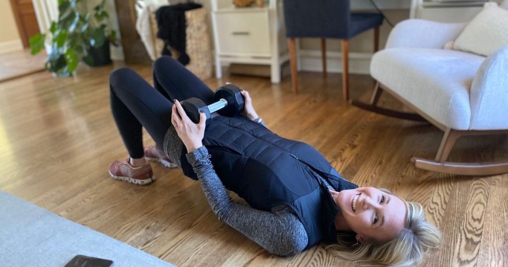 Woman laying on the floor doing glute bridges with a dumbell