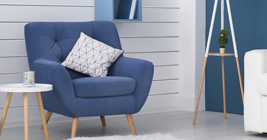 blue chair with a white colored pillow and end table sitting in a room with white shiplap on the back wall 