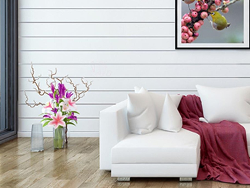 modern white couch with mauve throw and pillows next to vase of flowers and white shiplap on the back wall of the room 