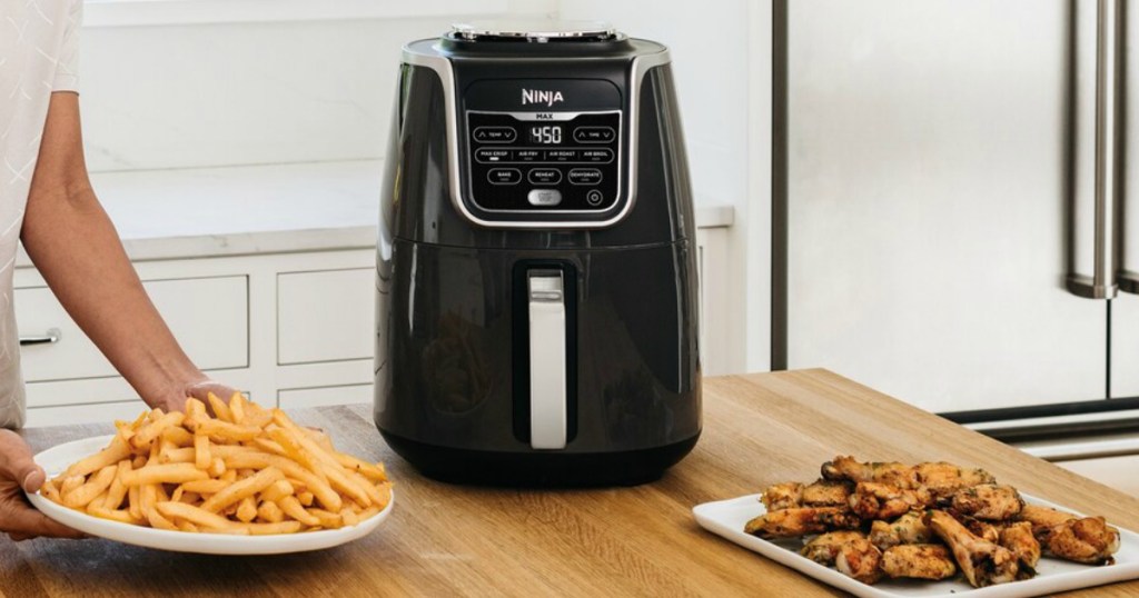 Woman grabbing a plate of fried foods near an air fryer on the counter