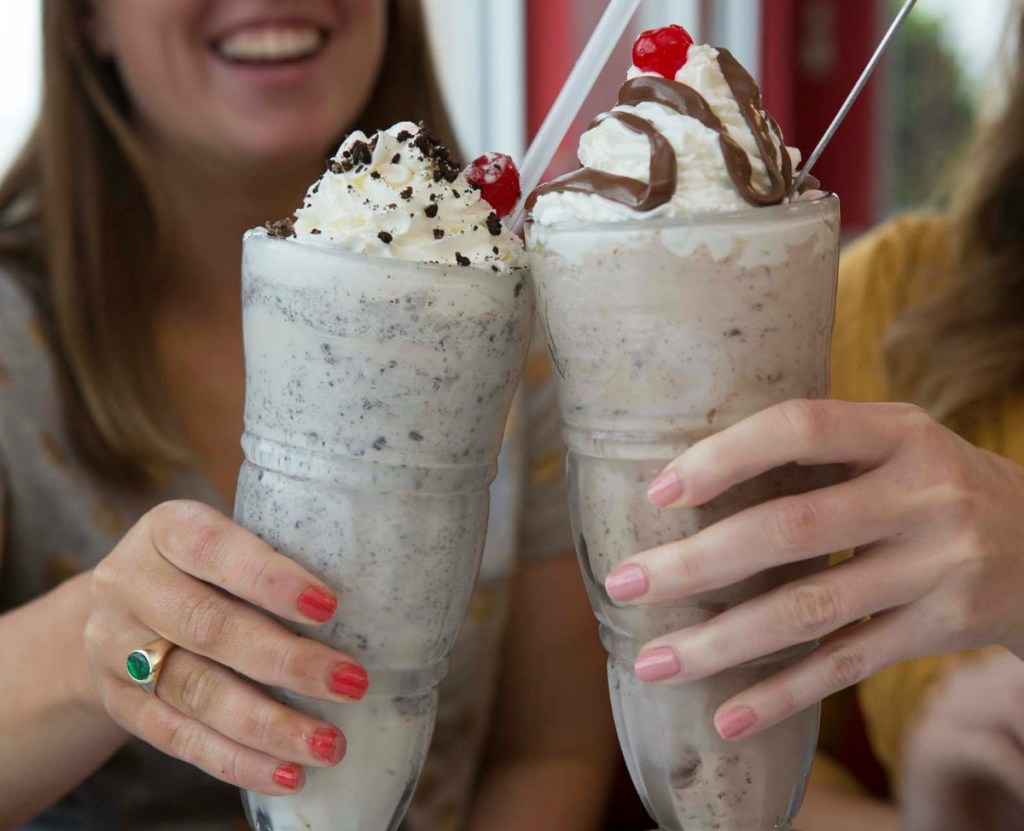 two women holding up milkshakes in glasses