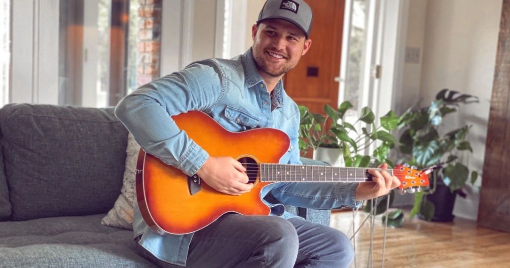 Man sitting on couch playing the guitar and smiling