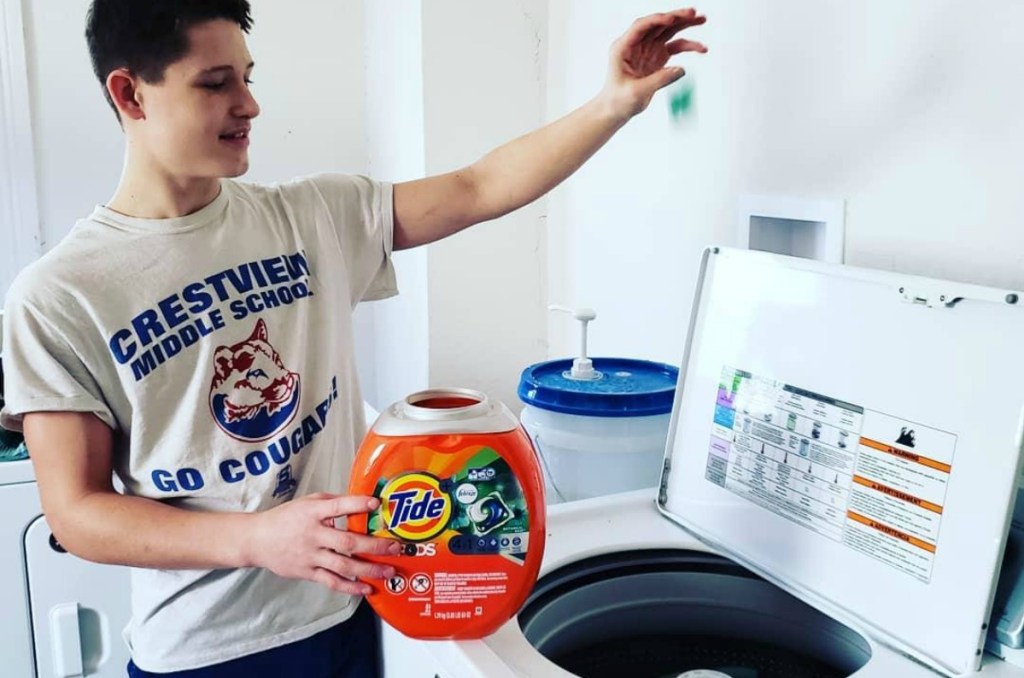 young man dropping a Tide POd into a washing machine