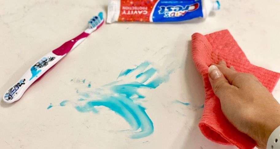 Hand using a Swedish Dishcloth to clean up a toothpaste mess in the bathroom