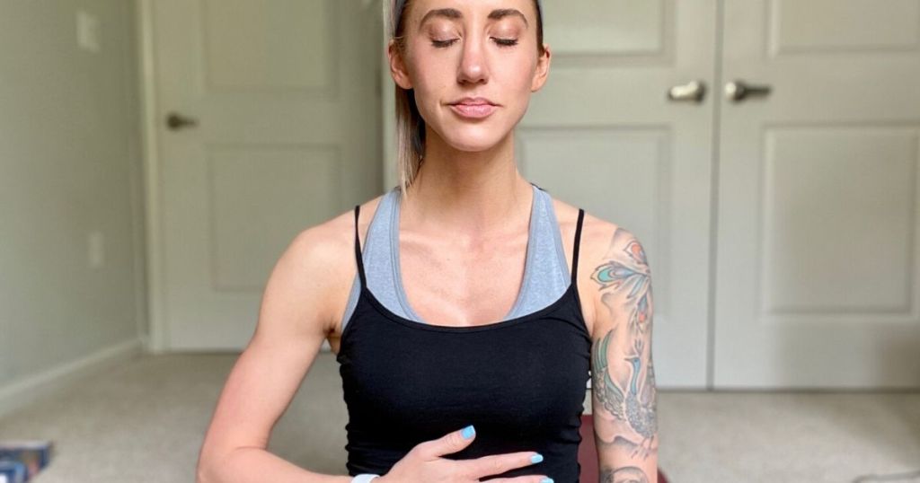 Woman sitting on the floor meditating with eyes closed and hand on stomach