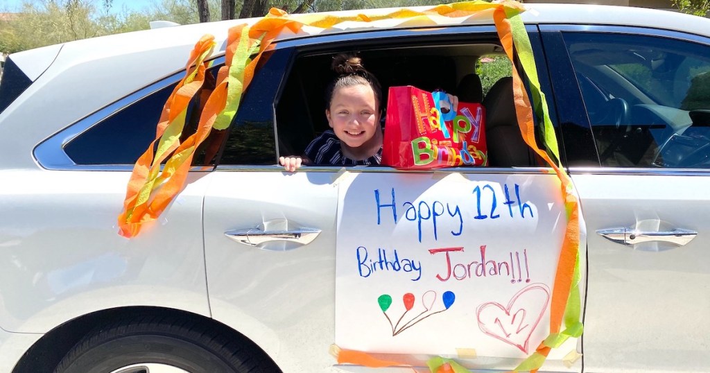 girl sitting in silver car with happy birthday poster on side with colorful streamers