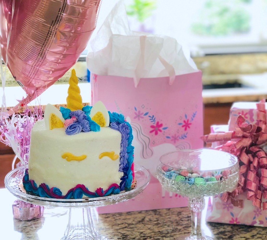 unicorn cake on glass stand with pink balloons and presents