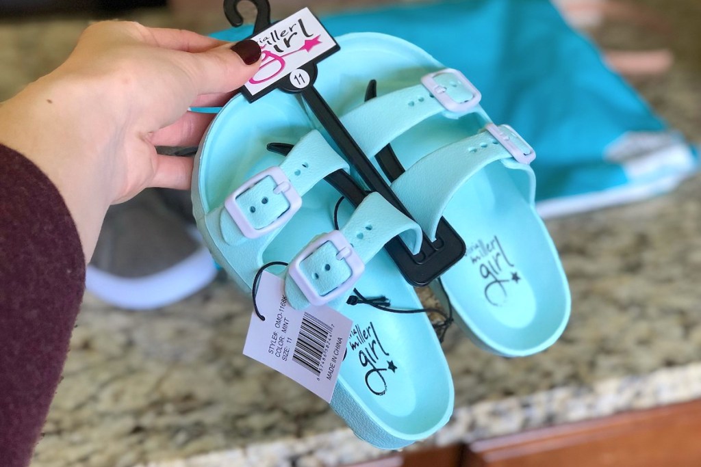 hand holding a pair of blue and white kids sandals on black hanger