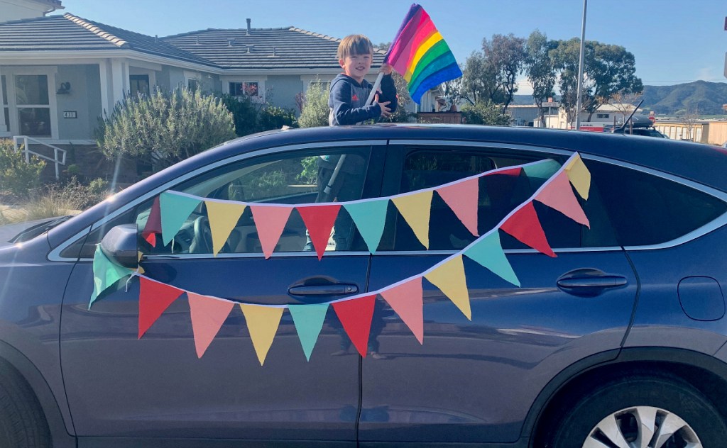 boy standing out of car holding rainbow flag