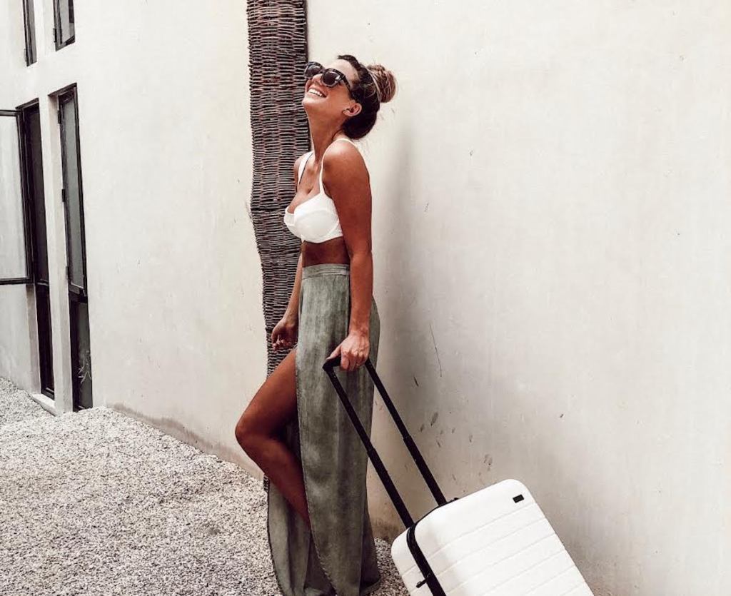 woman wearing sunglasses and bathing suit top with white luggage outside