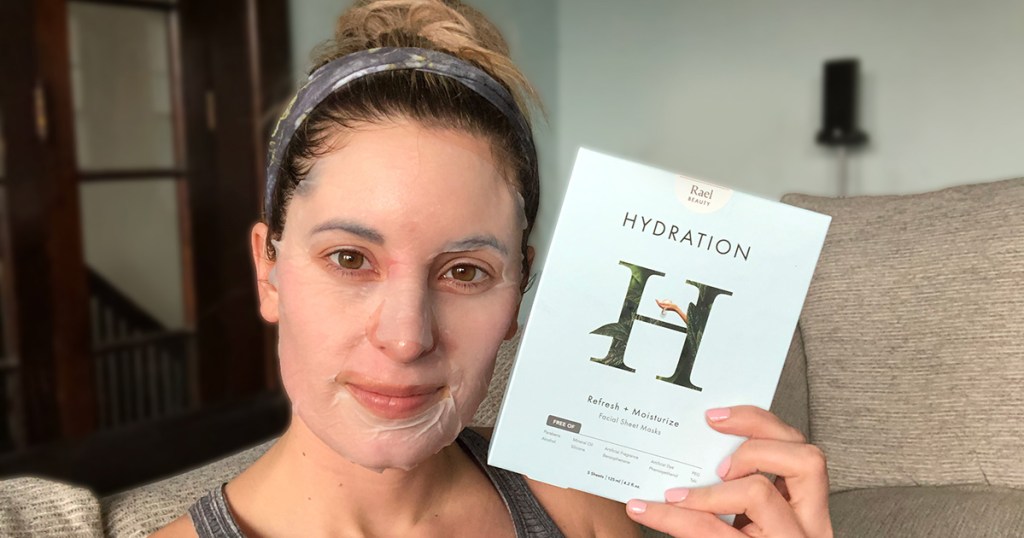 woman wearing sheet mask holding rael beauty mask box