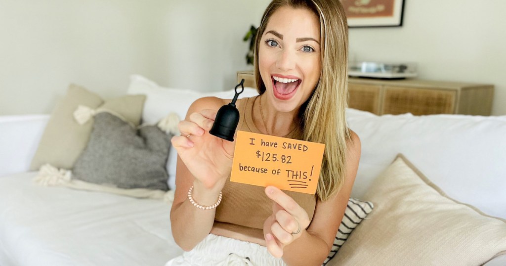 woman holding menstrual cup with savings sign sitting on couch