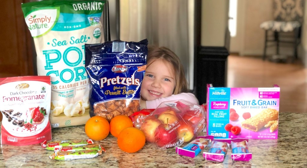 toddler girl smiling surrounded by tons of different snacks on counter