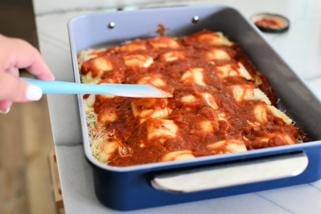 spreading marinara sauce onto ravioli casserole