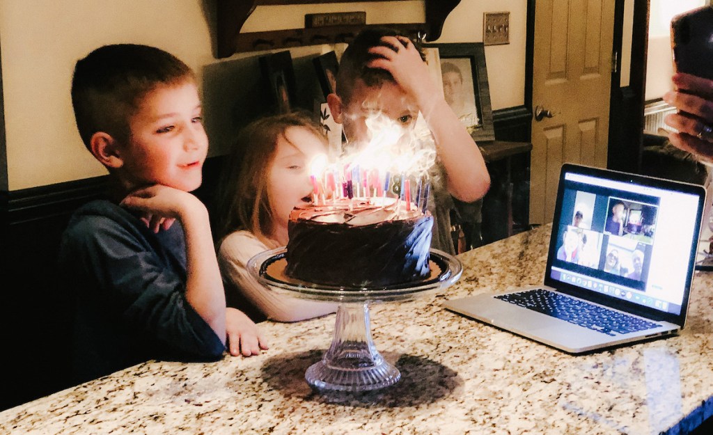 kids standing in front of cake with candles with onlineputer on granite countertop