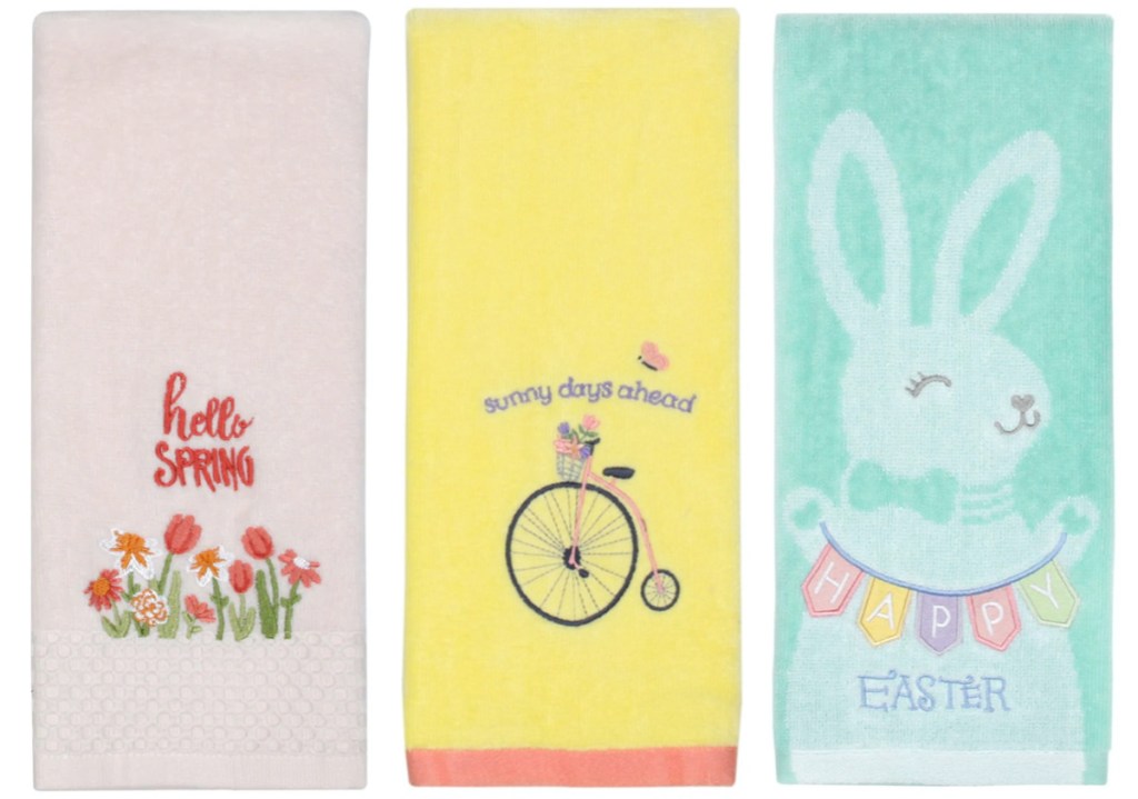 light pink hand towel with flowers that says "happy spring," yellow hand towel with bike that says "sunny days ahead," and blue Easter towel with bunny