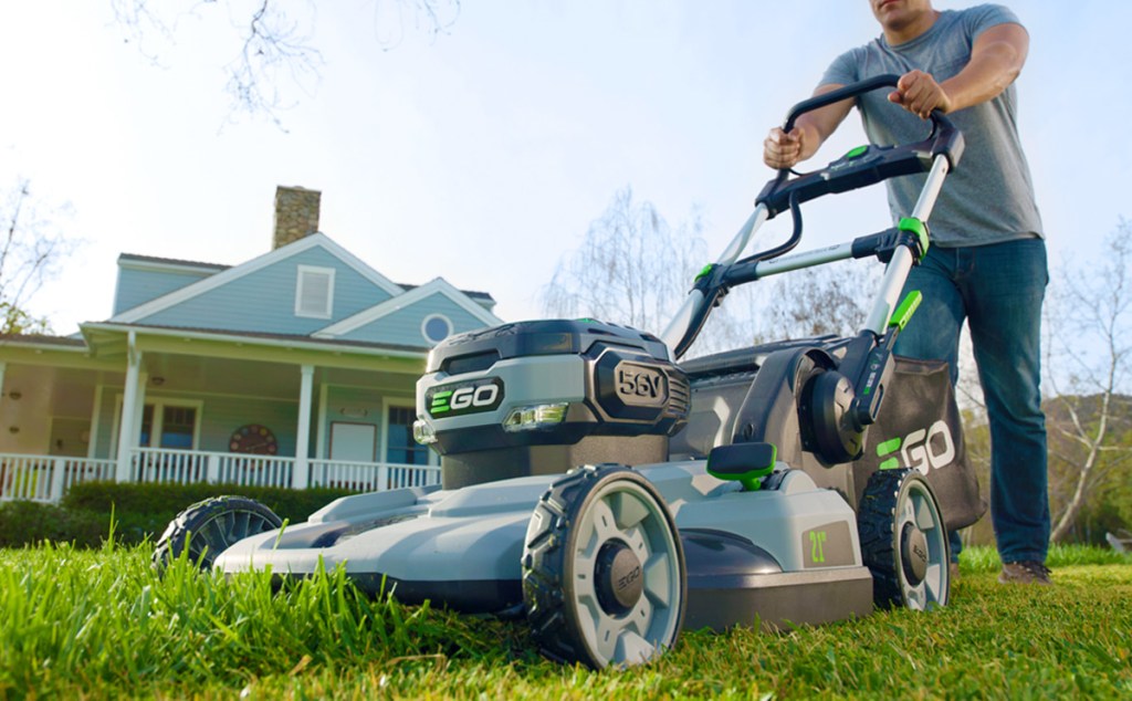 man pushing lawn mower across grass in front yard