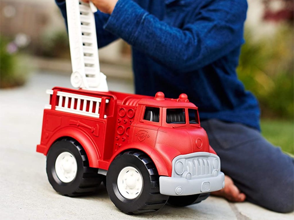 boy in blue shirt playing with red toy fire truck outside