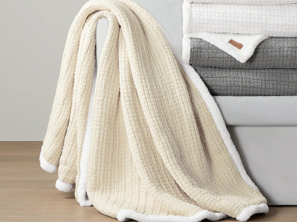 white trimmed cream throw blanket next to stack of white and grey throws