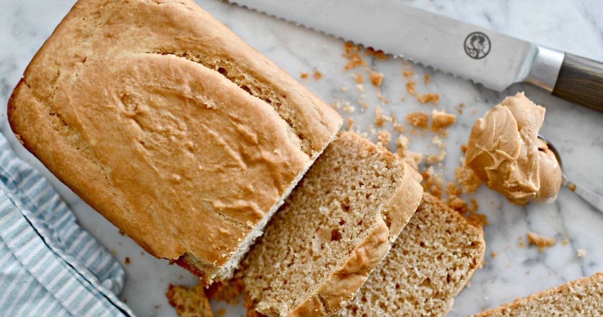 Sliced peanut butter bread on a cutting board next to a knife and spoonful of peanut butter