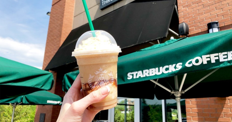 person holding starbucks frappuccino up outside of starbucks store