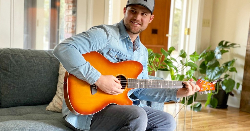 man in blue shirt sitting on couch playing guitar