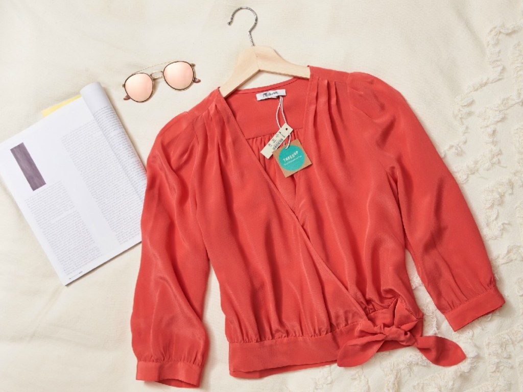 women's blouse displayed on bed next to sunglasses