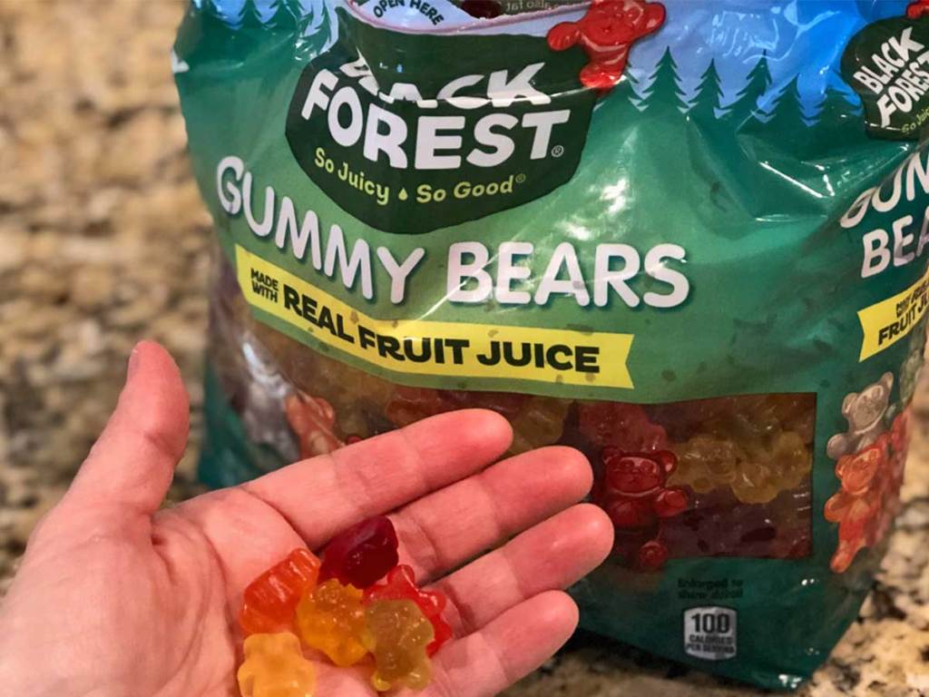 person holding gummy bears near large bag