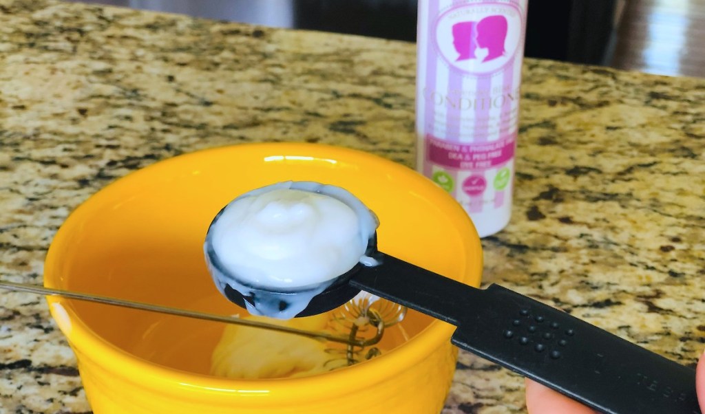 black measuring spoon with white conditioner over yellow bowl