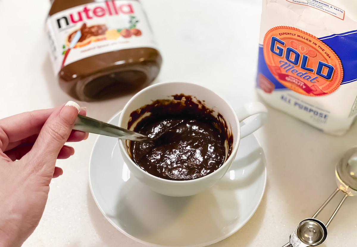 hand holding a spoon mixing brown cake batter in cup