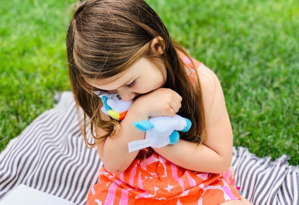 girl holding a stuffed rainbow unicorn giving it a hug