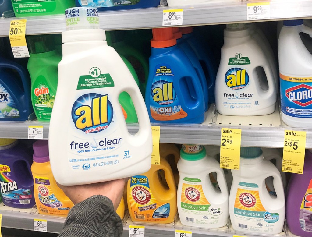 person holding up a white bottle of all laundry detergent in front of store shelf