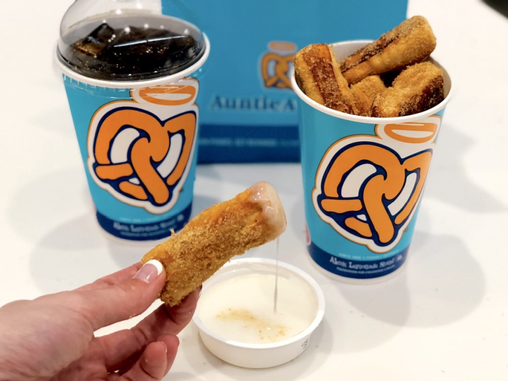 woman dipping pretzel bite in sweet dip, bucket of pretzel bites, and soda