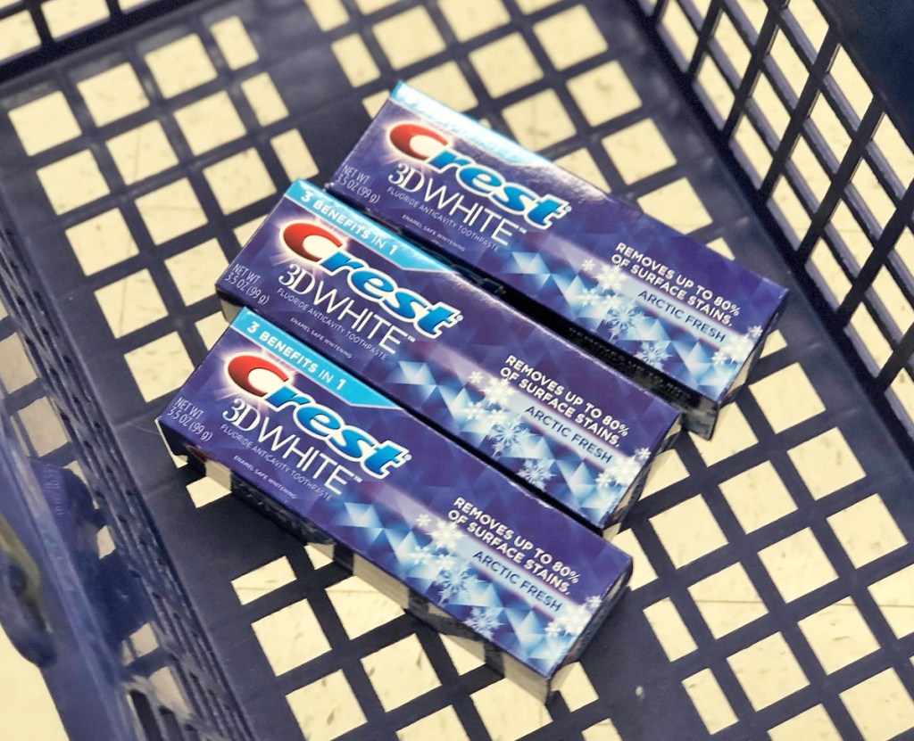 three blue boxes of crest 3d white toothpaste inside the bottom of a blue shopping basket