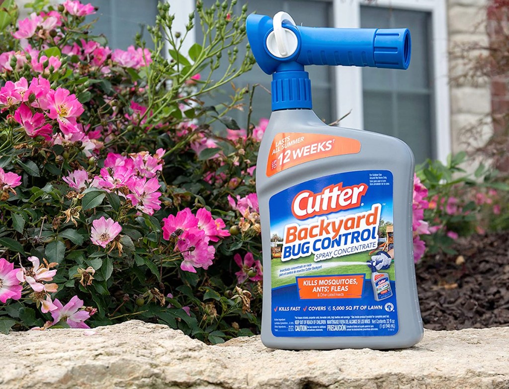 blue bottle of cutter backyard bug control sitting on stone wall next to pink flowers