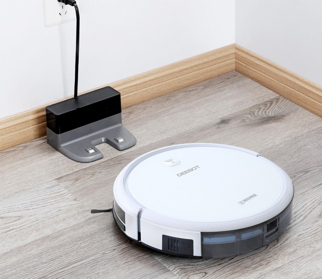 white robot vacuum on hardwood floor heading back to it's charging station