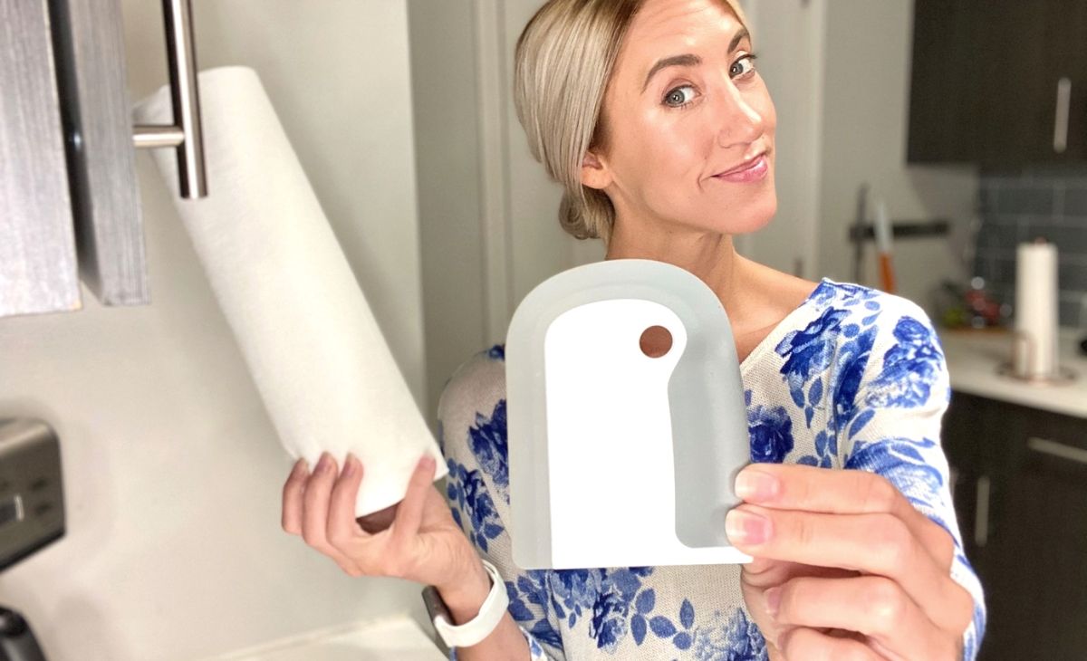 Woman holding oxo dish squeegee in one hand and a roll of paper towels in the other hand