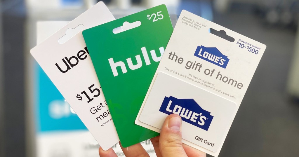 person holding three uber, hulu, and lowe's gift cards in hand