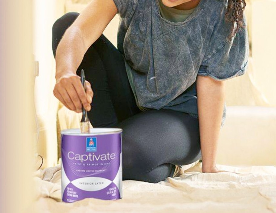 woman kneeling down and sticking paint brush into purple container of paint