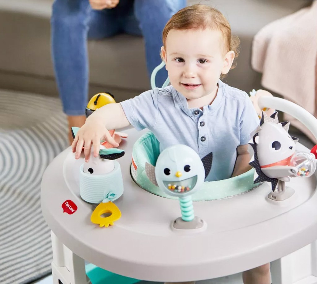 baby seating in grey rolling activity center with toys attached