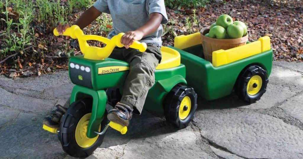 child on john deere rideon tractor toy with wagon in back carrying apples in a basket