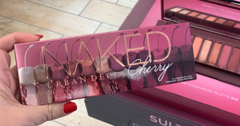 manicured hand holding eyeshadow palette in front of makeup display