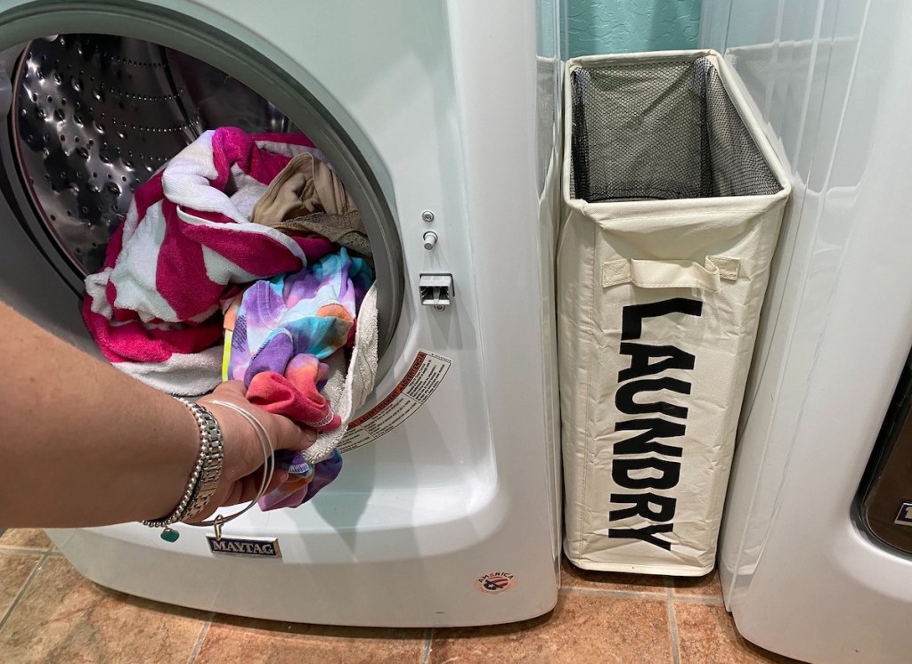 hand pulling out laundry from washer with laundry basket next to it