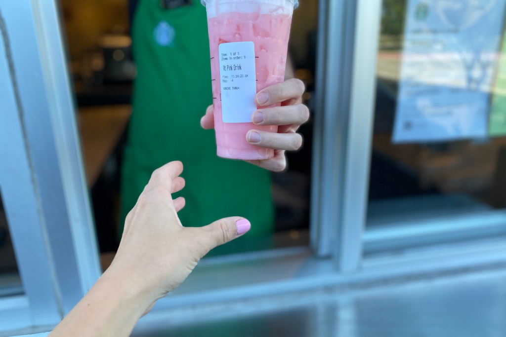 hand reaching for starbucks pink drink through the drive thru