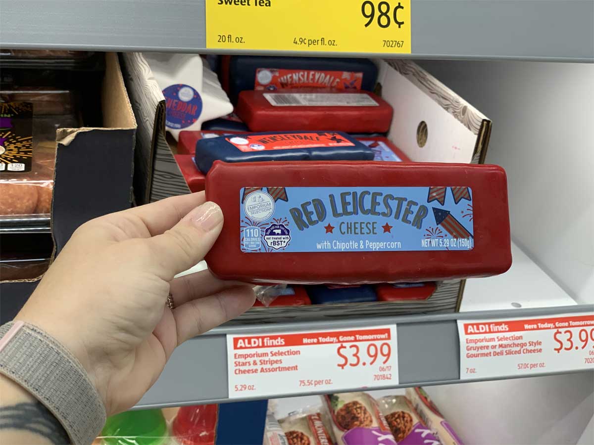 hand holding a block of cheese in red wax in front of a store display