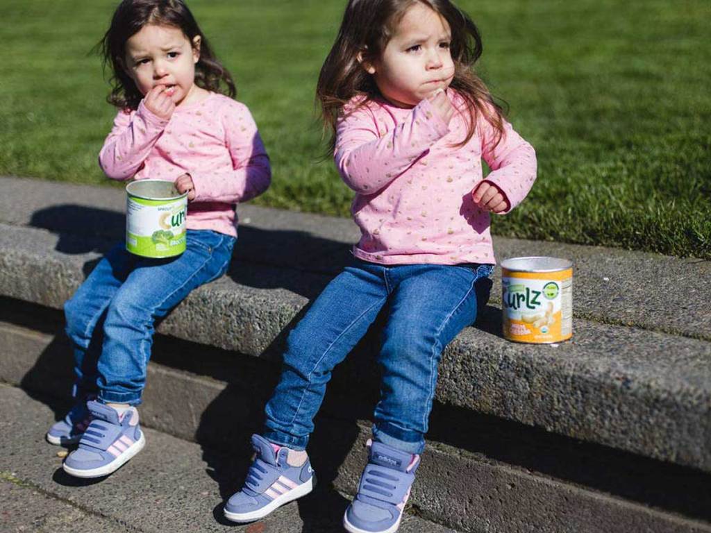 twin girls sitting on a ledge eating snacks