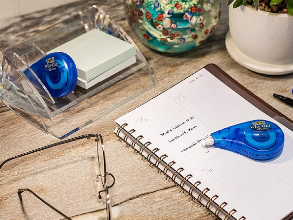 blue wite-out tape on desk with notebook, glasses, and more