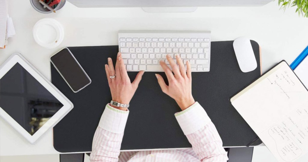 woman sitting at desk with black leather pad under her white wireless keyboard and mouse