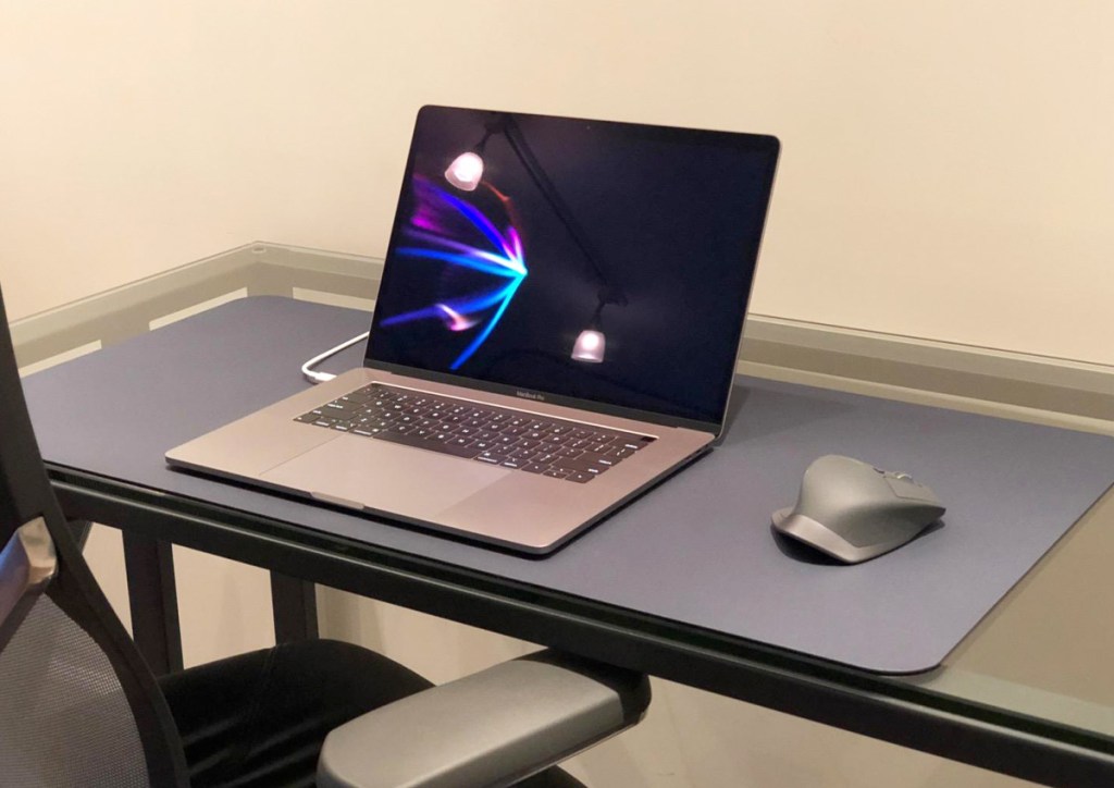 glass desk with blue leather pad on top with laptop on and mouse on top