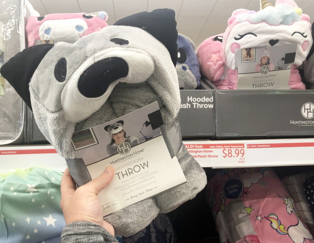 person holding up dog shaped kids hooded throw blanket next to shelf with more blankets in background